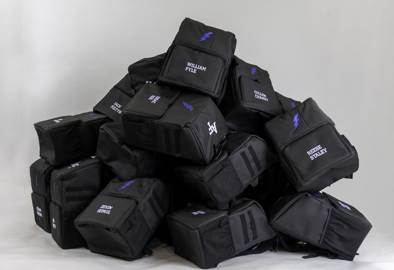 A production run of custom team backpacks stacked in a studio